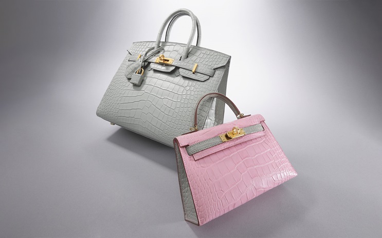 Two crocodile leather handbags, one gray and one pink, are displayed on a plain background.