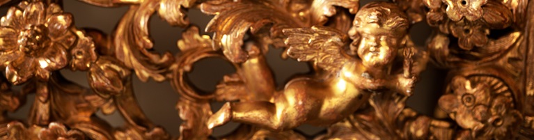 A gold ornamental carving featuring a cherub surrounded by intricate floral designs.
