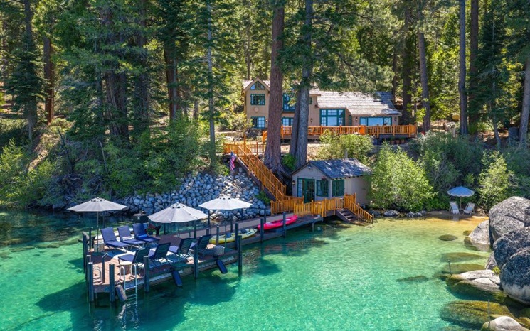 A cozy lakeside cabin with a dock, clear turquoise water, and surrounded by tall pine trees.