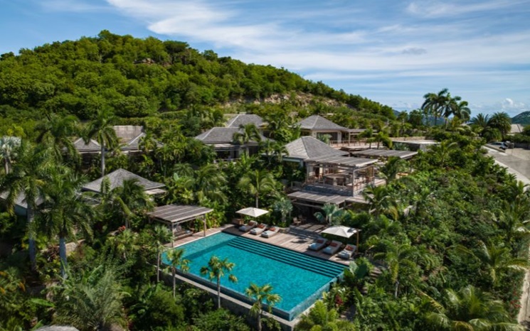 Luxury villas surrounded by lush greenery with infinity pool and lounge areas nestled on a hillside.
