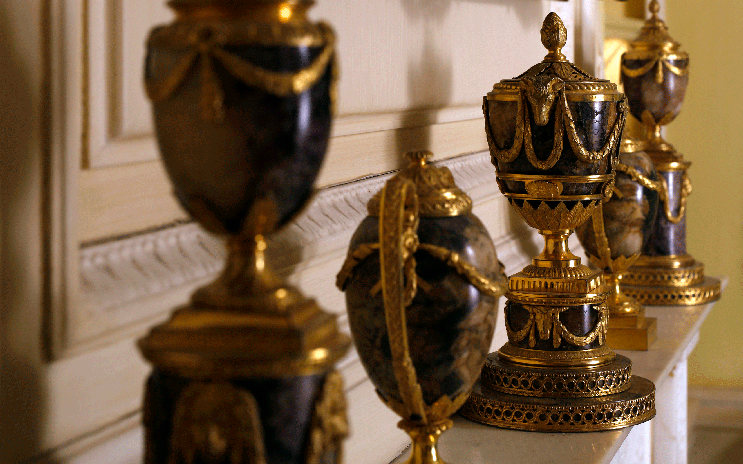Ornate decorative urns with gold accents are arranged on a mantelpiece.