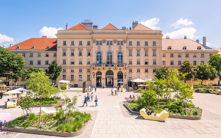 A large historic building with a central courtyard, greenery, and people walking around.