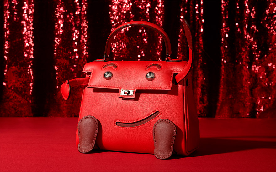 A red handbag with decorations resembling a smiling face and limbs is set against a red background.