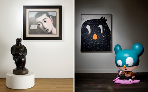 A dark, abstract statue sits on a white pedestal beneath a framed, blurred painting on a wall.