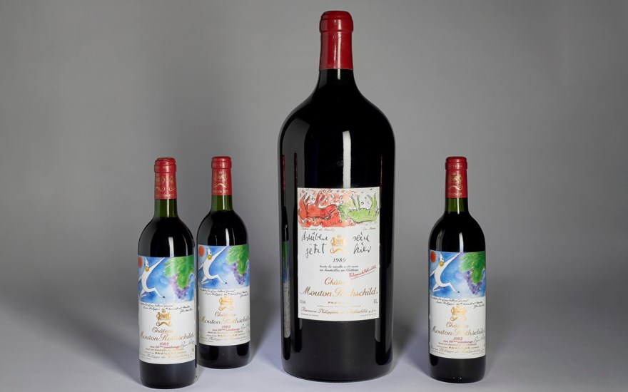 Four wine bottles of different sizes with red caps and colorful labels are displayed.