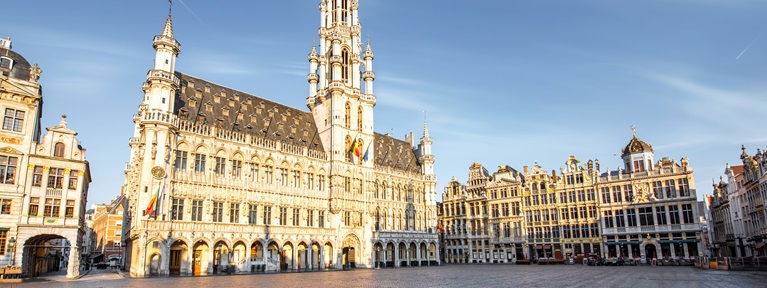 A grand square features ornate historic buildings under a clear blue sky in Brussels, Belgium.