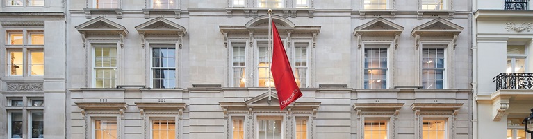 The image shows a classical building facade with multiple windows and a red flag hanging from a pole.