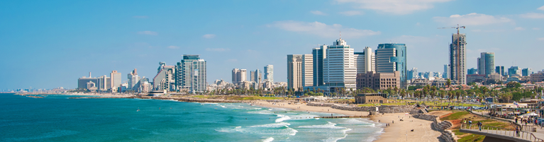 Panoramic view of a modern coastal city skyline along a crowded beach under a clear blue sky.