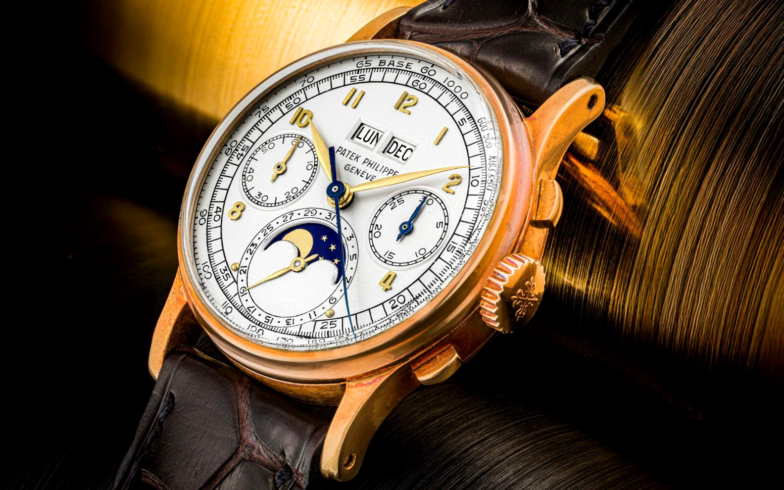 An elegant gold watch featuring multiple complications, including a moon phase indicator, set against a dynamic blurred background.