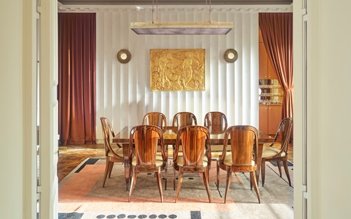 A formal dining room with a long table, eight chairs, and gold artwork on the wall.