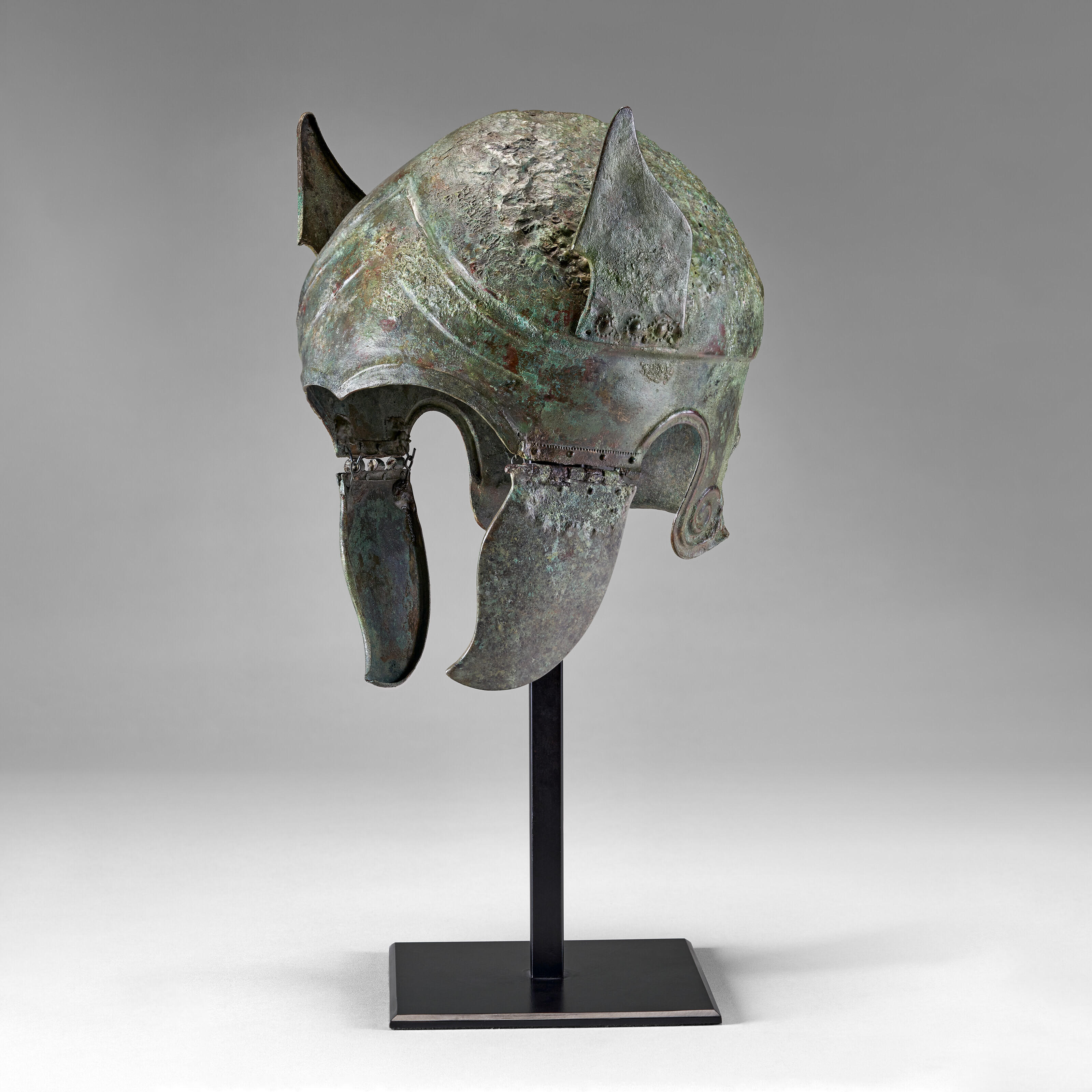 A GREEK BRONZE APULO-CORINTHIAN HELMET AND PAIR OF ANKLE-GUARDS